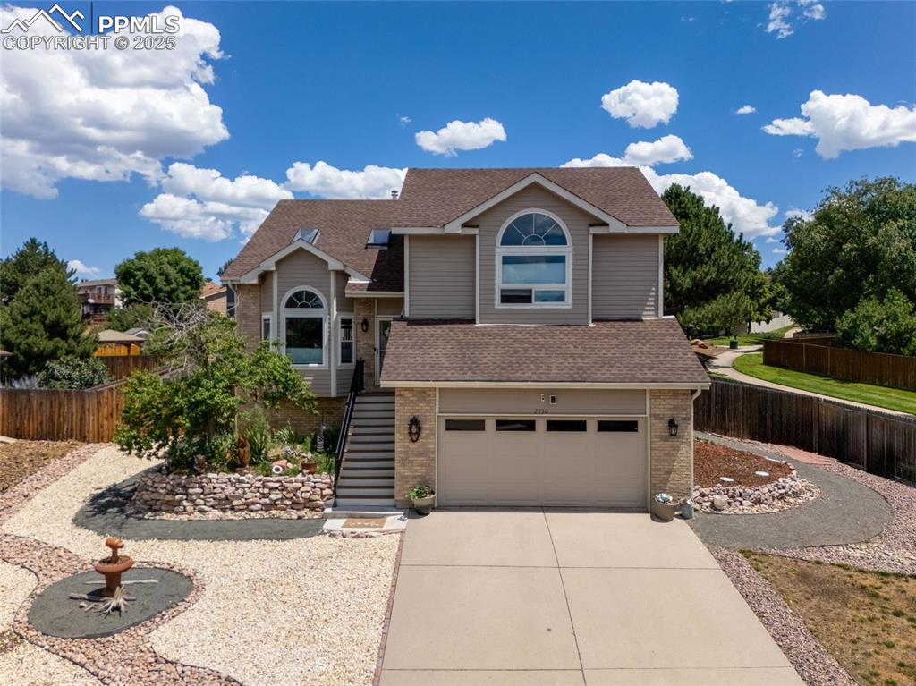 Caption: View of front of property with brick siding, roof with shingles, driveway, a garage, and stairs