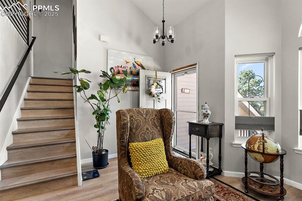 Image 10 of 41: Sitting room with high vaulted ceiling, stairway, a chandelier, and wood fi
