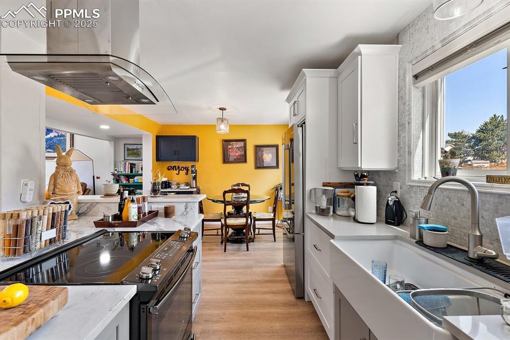 Image 15 of 41: Kitchen with island exhaust hood, range with electric stovetop, backsplash,