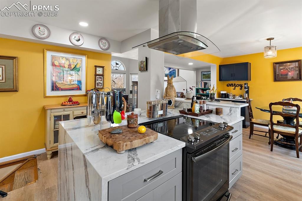 Image 16 of 41: Kitchen featuring black / electric stove, island range hood, light wood fin
