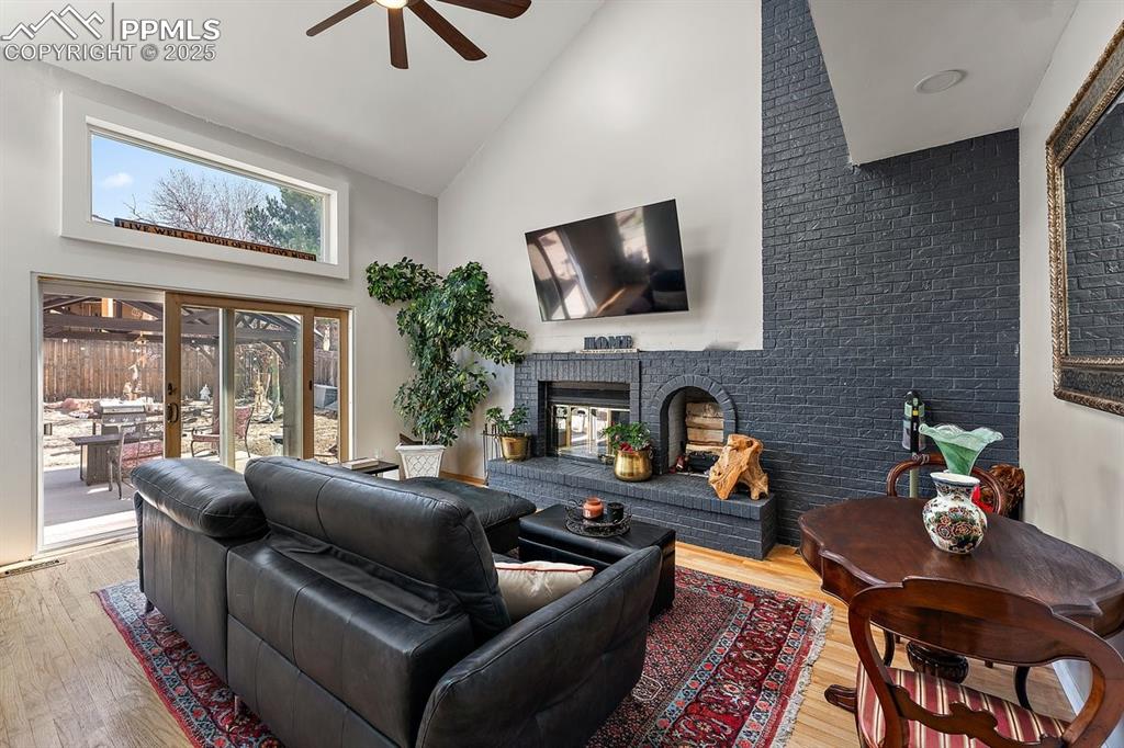 Image 19 of 41: Living room with high vaulted ceiling, ceiling fan, a brick fireplace, and 