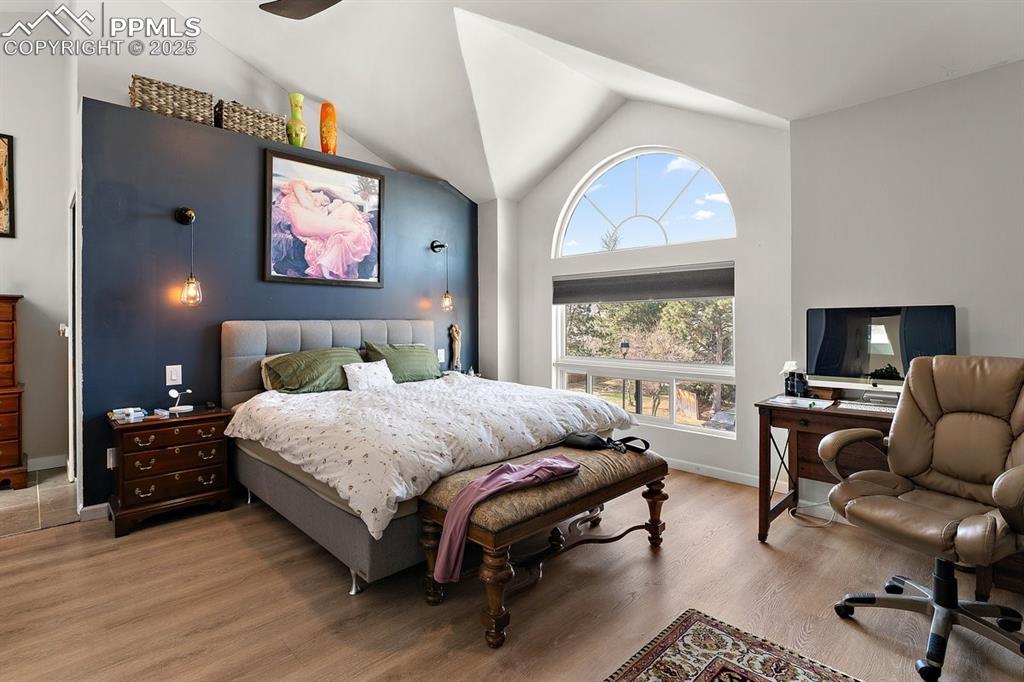 Image 24 of 41: Bedroom featuring wood finished floors, an office area, and high vaulted ce