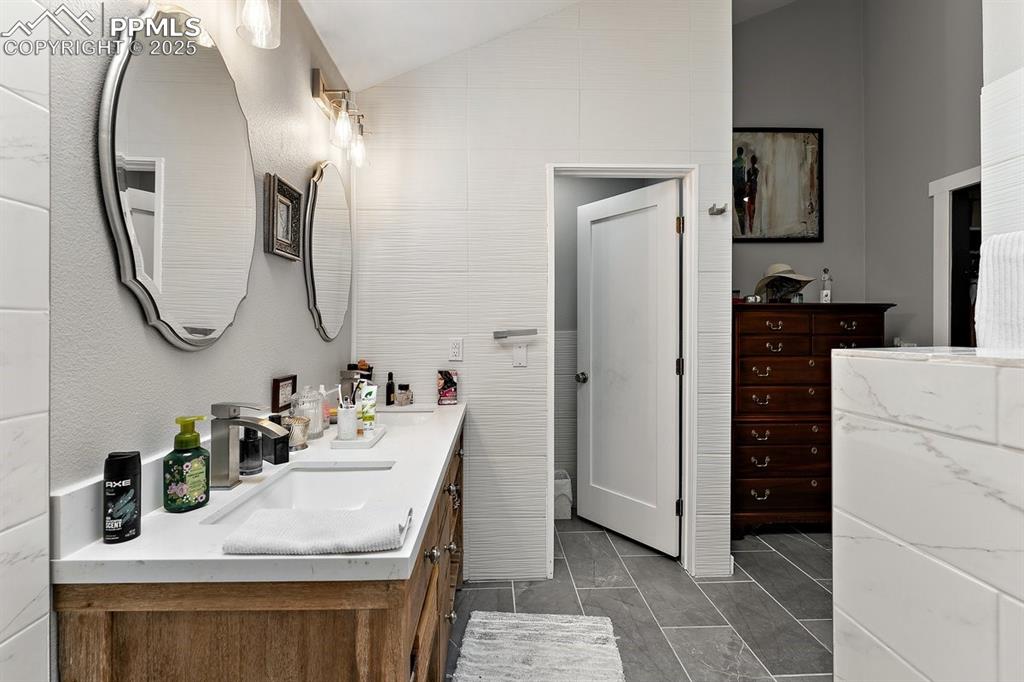 Image 28 of 41: Full bathroom featuring vaulted ceiling, double vanity, and marble look til