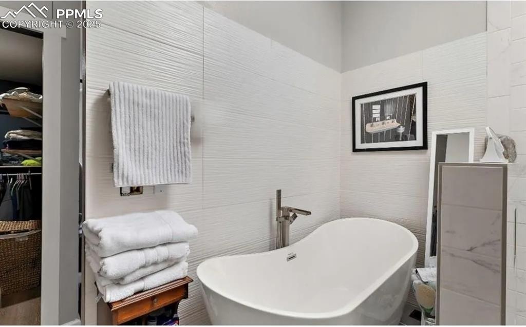 Image 29 of 41: Bathroom featuring tile walls, a freestanding tub, and a walk in closet
