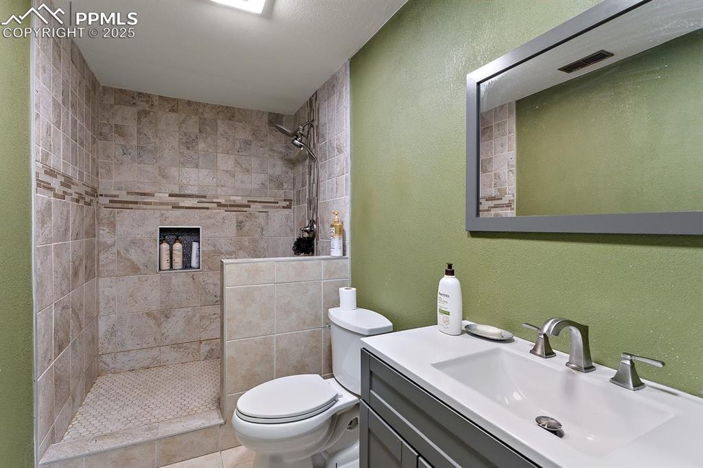 Image 39 of 41: Full bath featuring a tile shower, vanity, and a textured wall