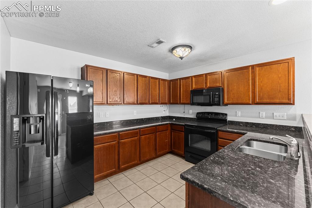 Image 12 of 30: Kitchen featuring black appliances, light tile patterned floors, dark stone
