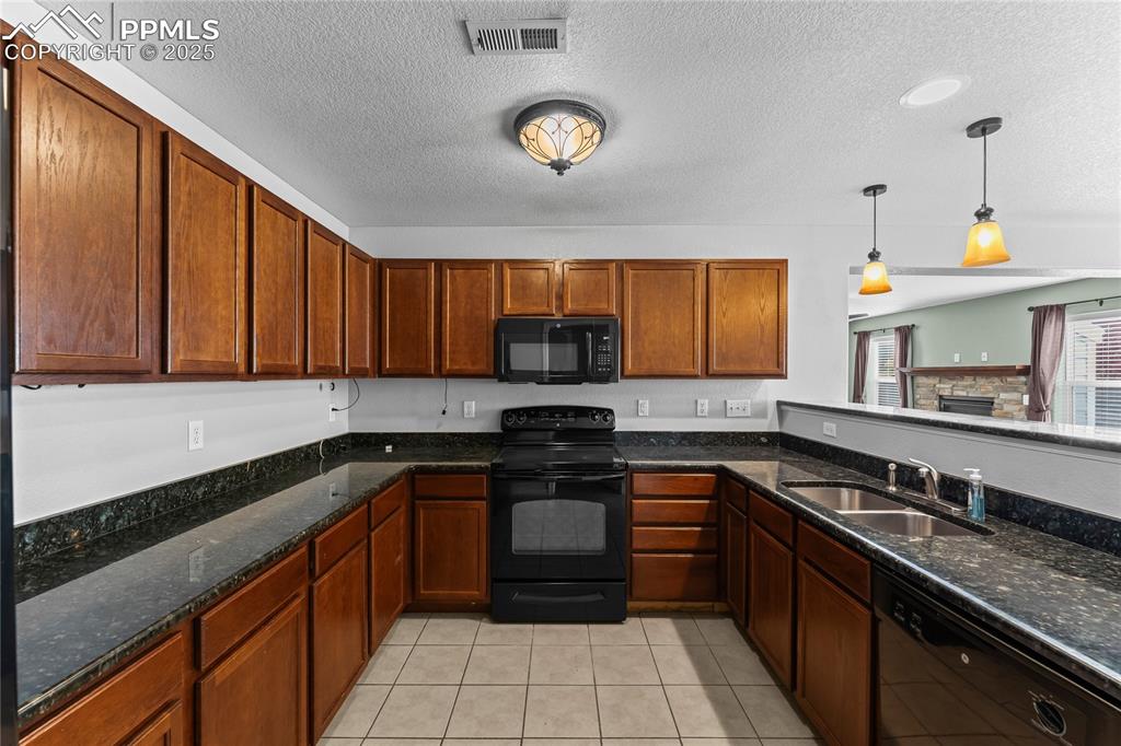 Image 13 of 30: Kitchen featuring black appliances, decorative light fixtures, dark stone c