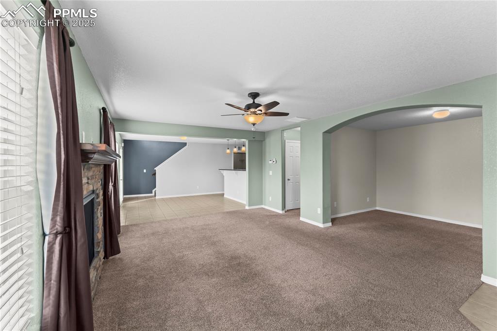 Image 6 of 30: Unfurnished living room with light carpet, a stone fireplace, arched walkwa