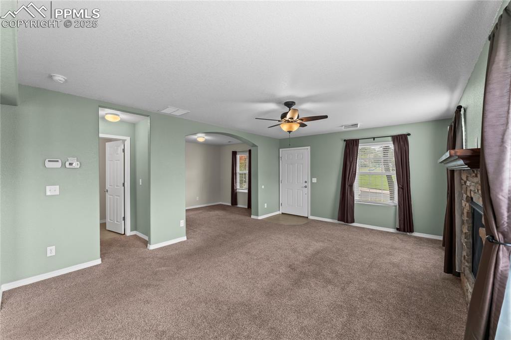 Image 8 of 30: Unfurnished living room with arched walkways, carpet floors, a stone firepl