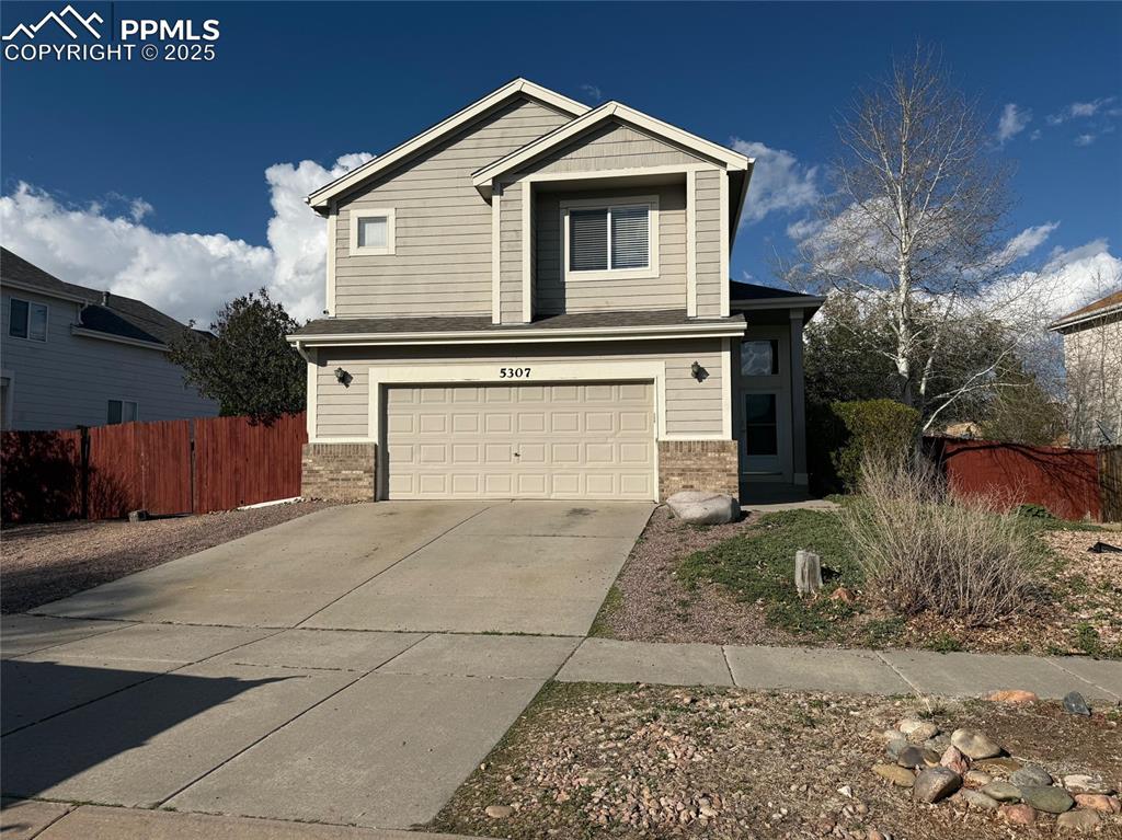 Caption: View of front of property with brick siding, an attached garage, and driveway