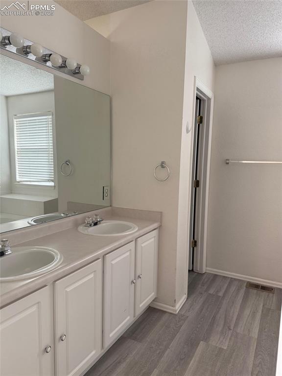 Image 13 of 34: Full bathroom with a textured ceiling, double vanity, wood finished floors,