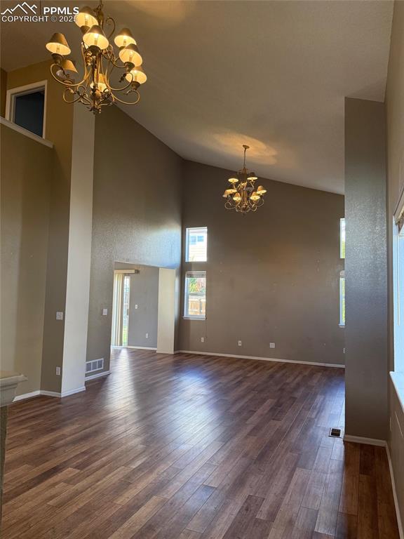 Image 2 of 34: Spare room with a chandelier, high vaulted ceiling, wood finished floors, a