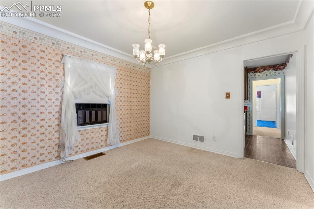 Image 10 of 30: Unfurnished living room with carpet, a chandelier, ornamental molding, and
