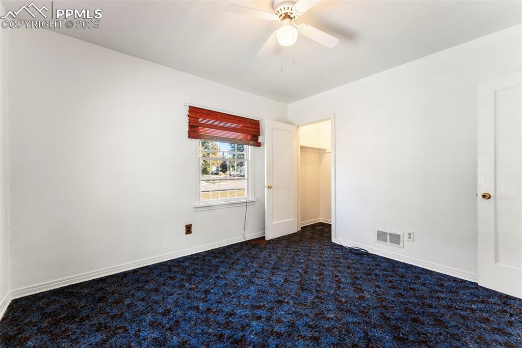 Image 13 of 30: Unfurnished bedroom with dark carpet, a walk in closet, and a ceiling fan