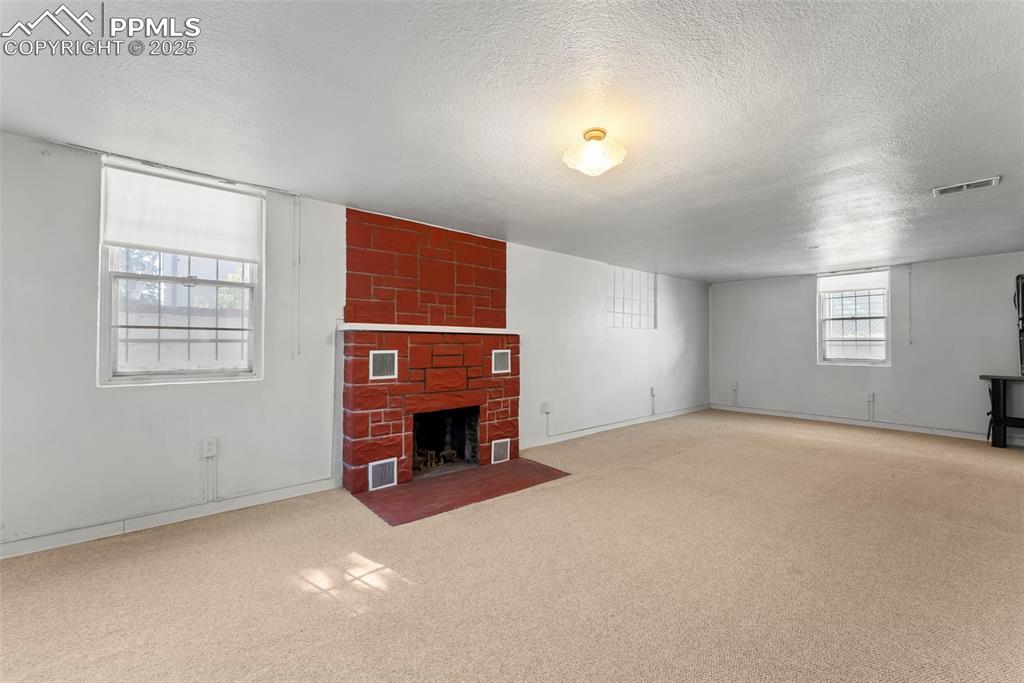 Image 16 of 30: Unfurnished living room featuring a fireplace, a textured ceiling, and carp