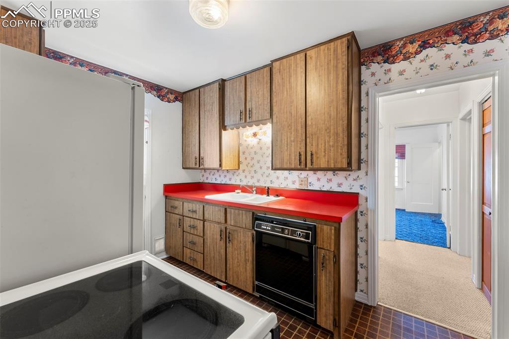 Image 4 of 30: Kitchen with wallpapered walls, dark colored carpet, dishwasher, brown cabi