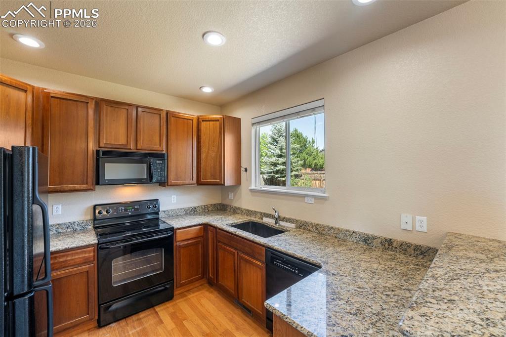 Image 10 of 39: Kitchen featuring black appliances, wood finish cabinets, light stone count