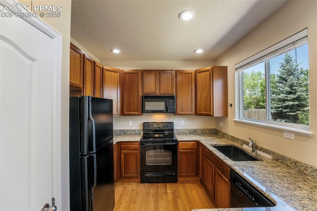 Image 11 of 39: Kitchen with black appliances, wood finish cabinetry, light stone counters,