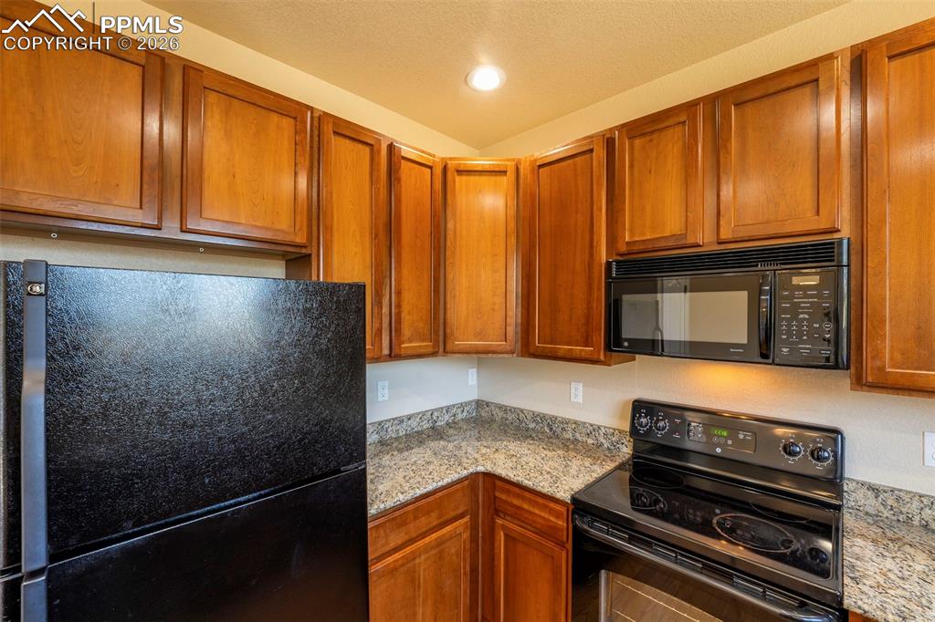 Image 13 of 39: Kitchen with black appliances, wood finish cabinetry, light stone counterto
