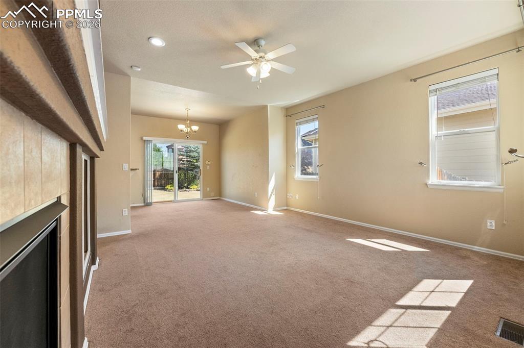 Image 7 of 39: Unfurnished living room with a ceiling fan, hanging lights, carpet, and a t
