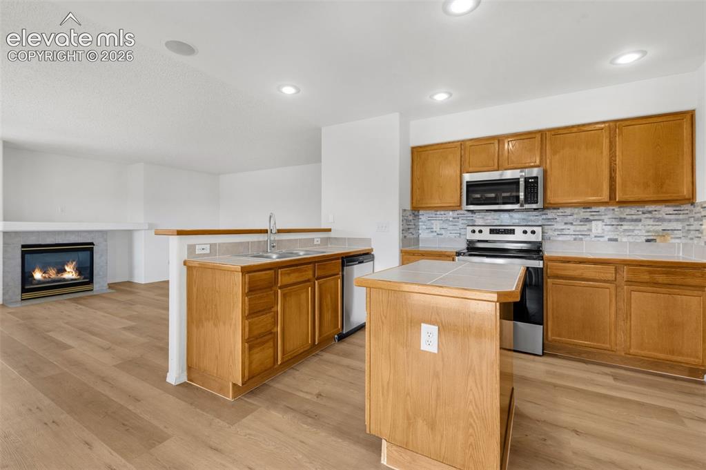 Image 12 of 48: Kitchen with wood-finish flooring, recessed lighting, wood cabinetry, stain