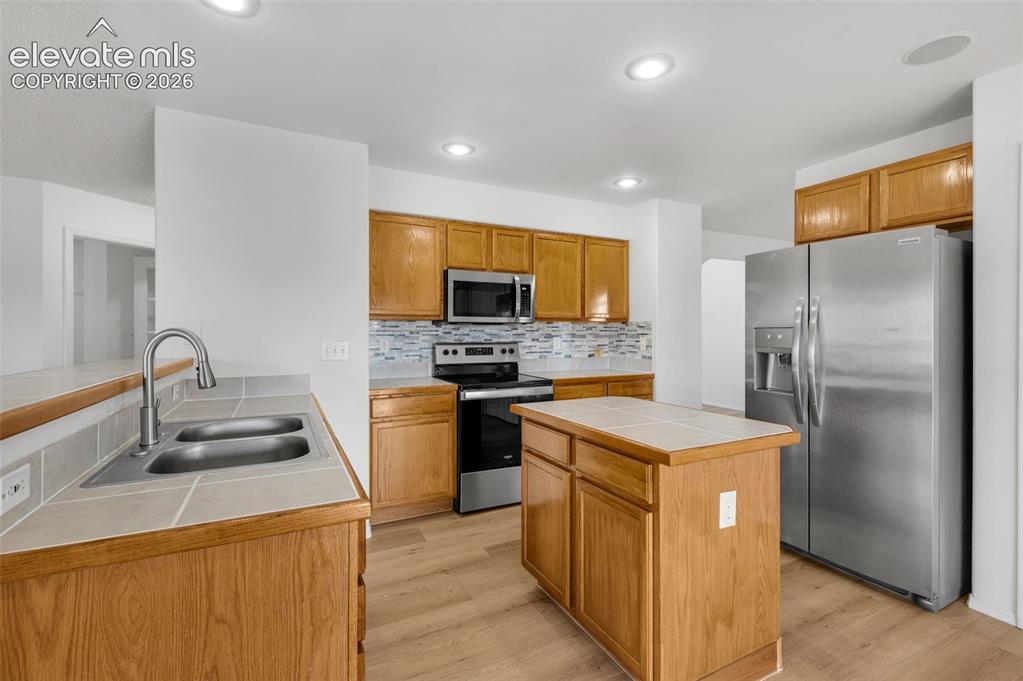 Image 16 of 48: Kitchen featuring wood cabinetry, stainless steel appliances, a tiled backs