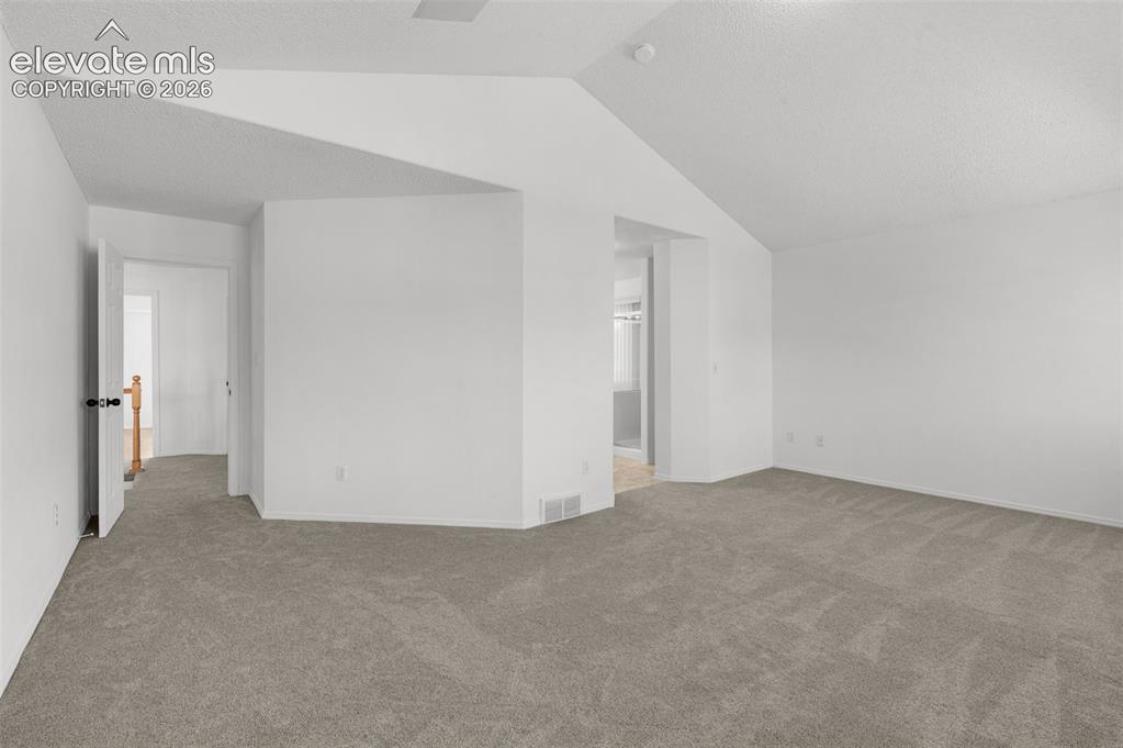 Image 21 of 48: Neutral-toned carpeting, white walls, and a vaulted ceiling
