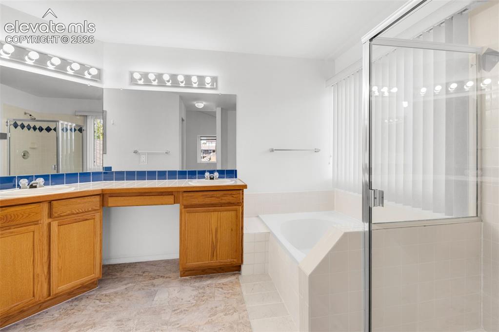 Image 24 of 48: Dual vanity with wood cabinetry, large mirrors, built-in soaking tub, glass