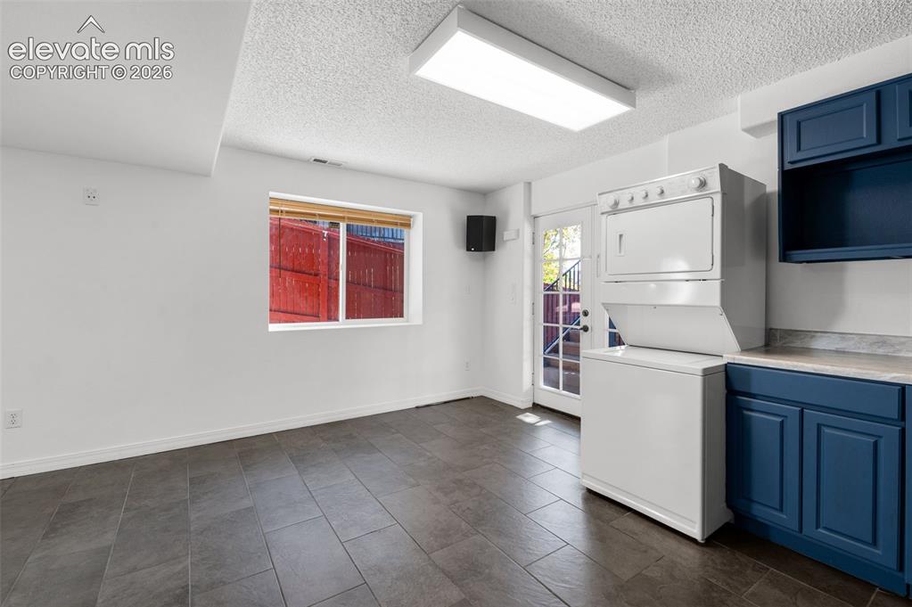 Image 36 of 48: Tile flooring, white walls, built-in blue cabinetry, white stackable washer
