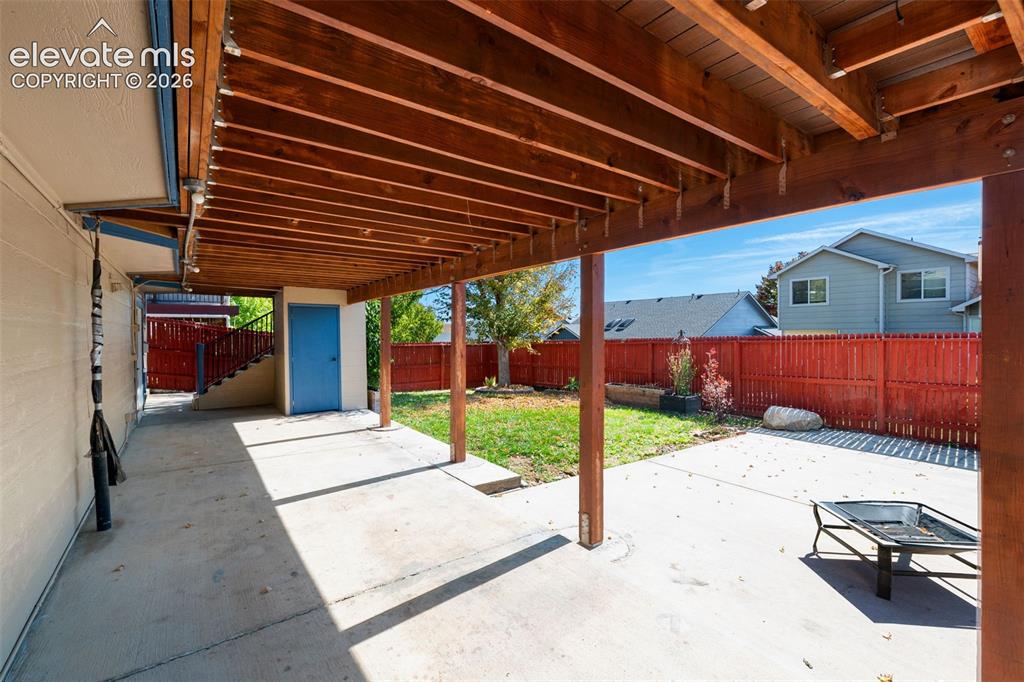 Image 45 of 48: Covered patio with exposed wood beams, concrete flooring, private storage a