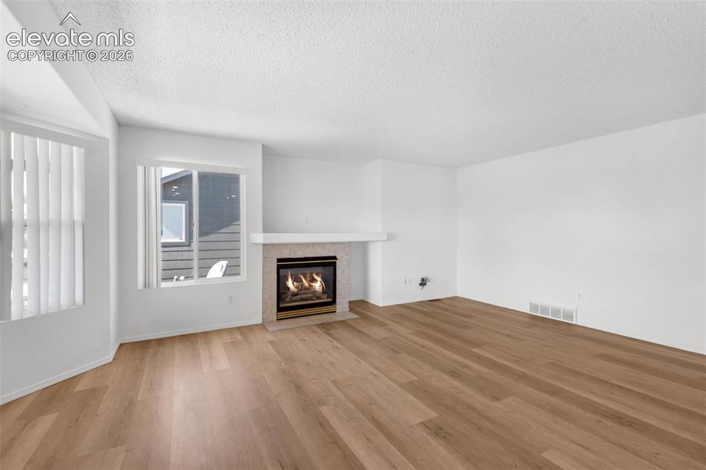 Image 9 of 48: Wood-finish flooring, white walls, and a fireplace with a light-toned tile