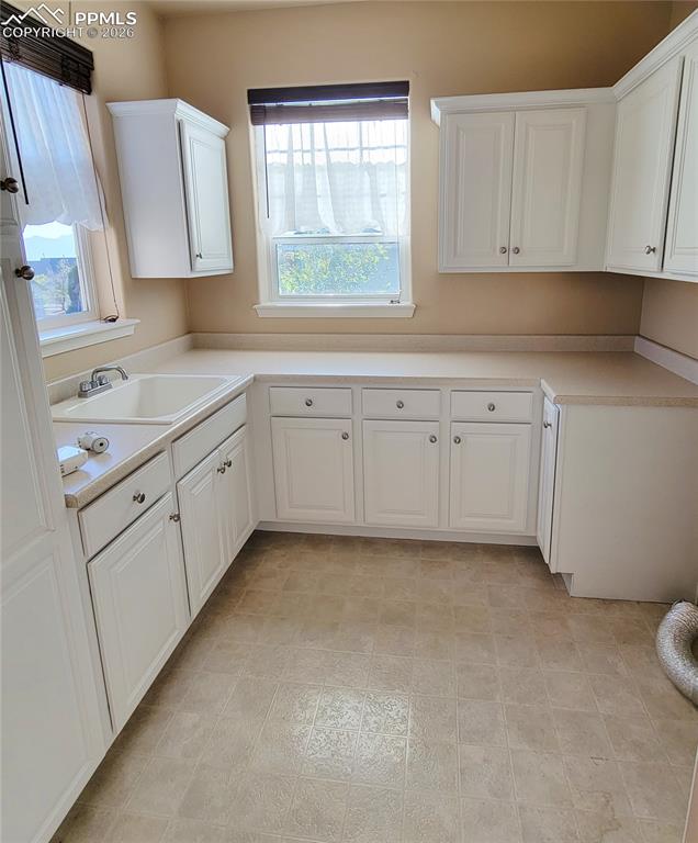 Image 27 of 38: Large laundry room with cabinetry, sink, and windows.