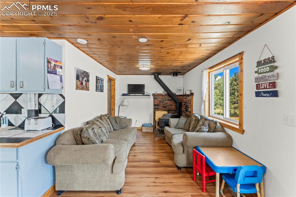 Image 10 of 30: Living room with a wood stove, wooden ceiling, and light wood-style floors