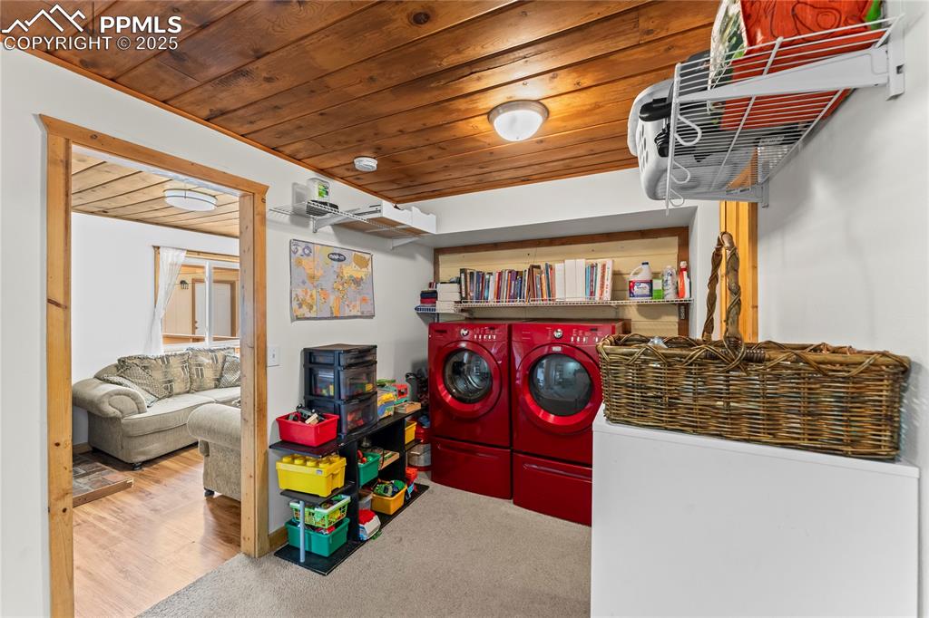 Image 16 of 30: Laundry room featuring wood ceiling, washer and clothes dryer, and carpet f