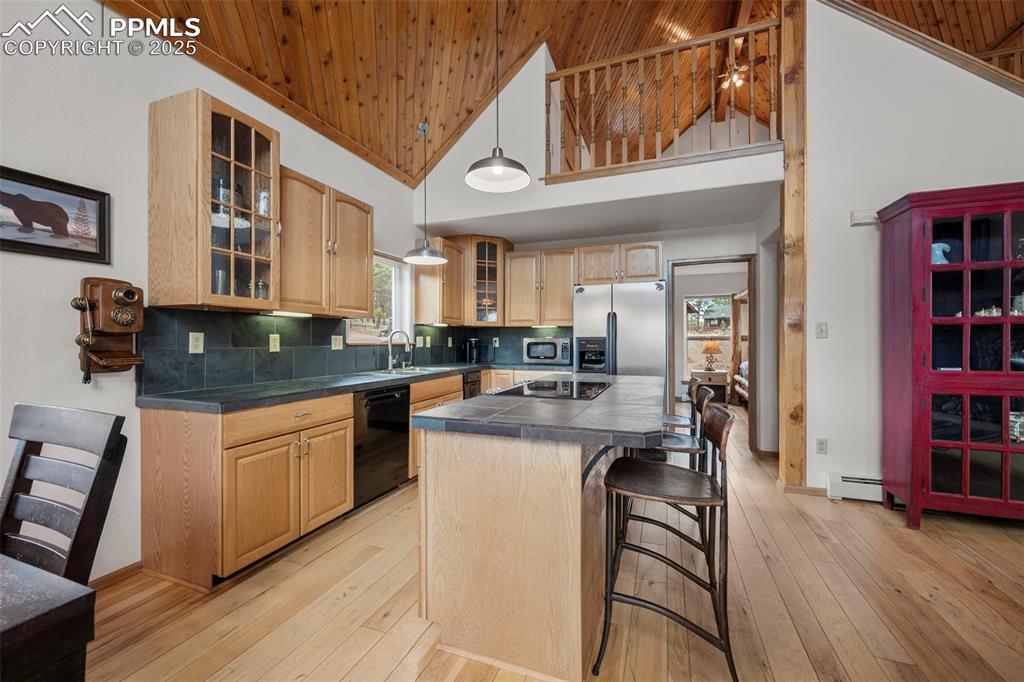 Image 9 of 38: Kitchen featuring a breakfast bar, tasteful backsplash, glass insert cabine
