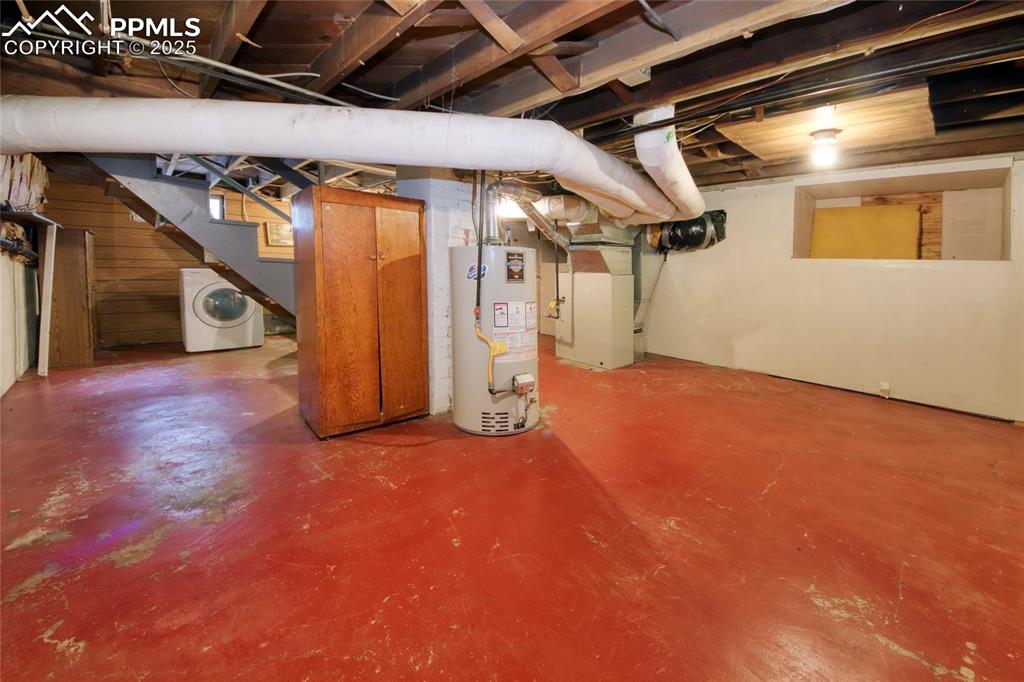 Image 21 of 28: Unfinished below grade area featuring water heater, washer / clothes dryer,