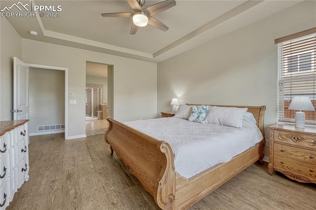 Image 11 of 47: Bedroom with a raised ceiling, light wood-type flooring, a ceiling fan, and