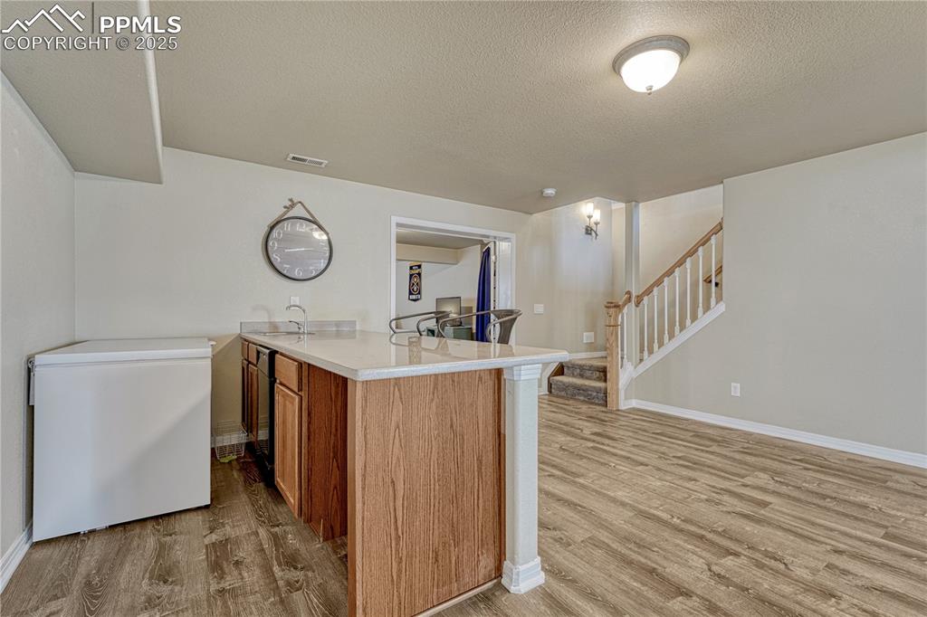 Image 25 of 47: Kitchen featuring a peninsula, brown cabinetry, a textured ceiling, light w