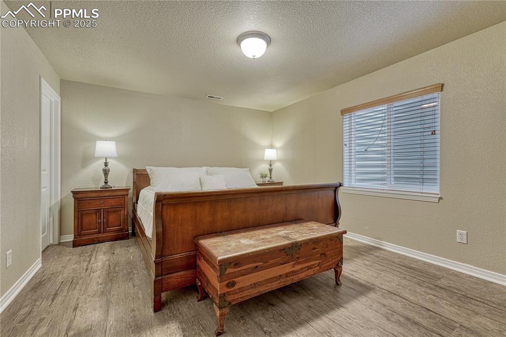 Image 32 of 47: Bedroom with a textured wall, light wood-style flooring, and a textured cei