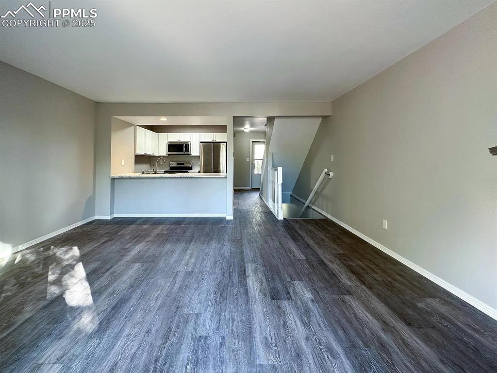 Image 10 of 23: Unfurnished living room featuring dark wood-style flooring, baseboards, and