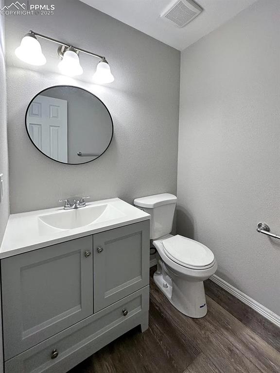 Image 4 of 23: Half bathroom with vanity, baseboards, toilet, visible vents, and wood fini