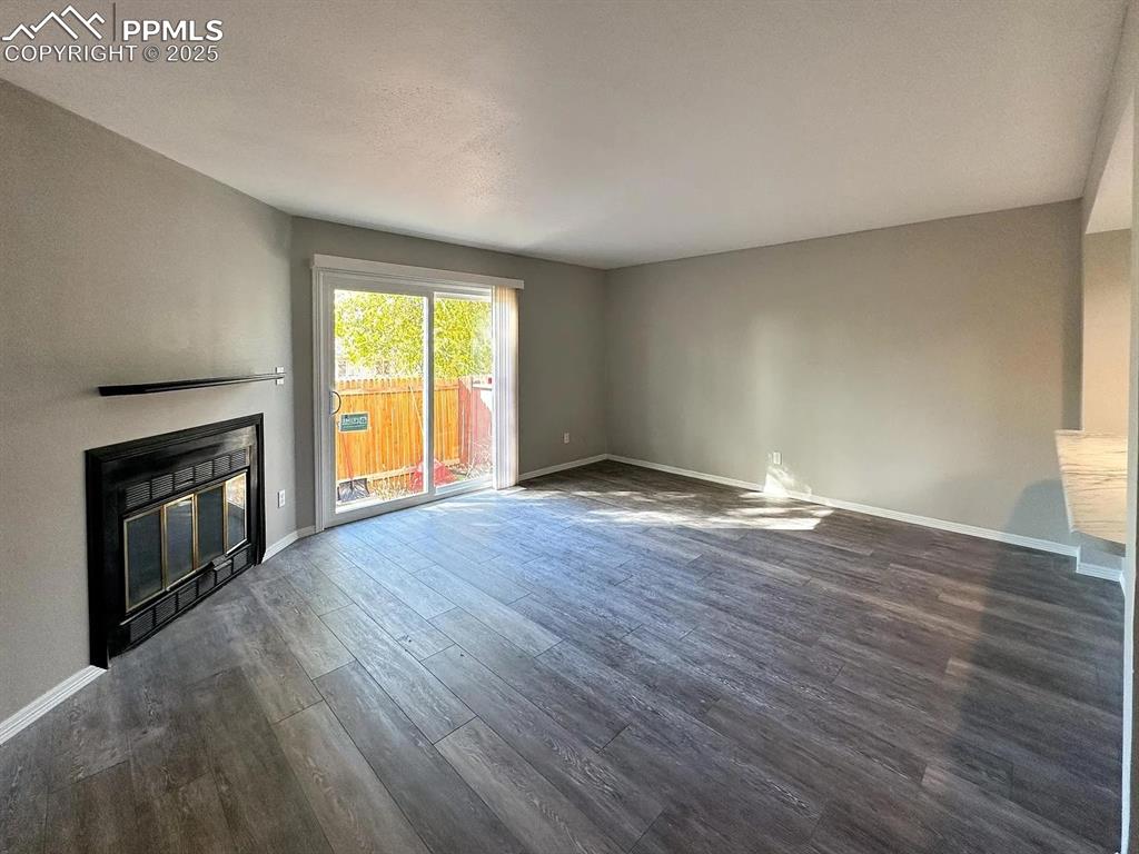 Image 9 of 23: Unfurnished living room featuring a glass covered fireplace, dark wood-type
