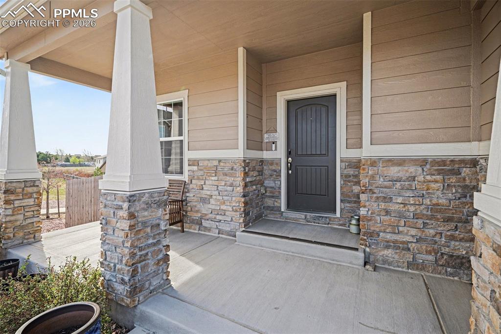 Image 3 of 40: Covered front porch featuring a dark entry door, stacked stone accents, hor