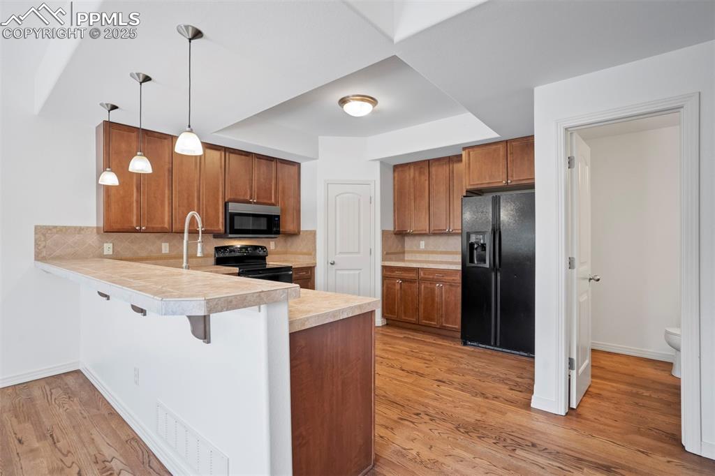 Image 10 of 50: Kitchen with a peninsula, backsplash, black appliances, light countertops,