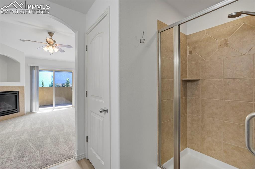Image 20 of 50: Full bathroom with a ceiling fan, a shower stall, and a tiled fireplace