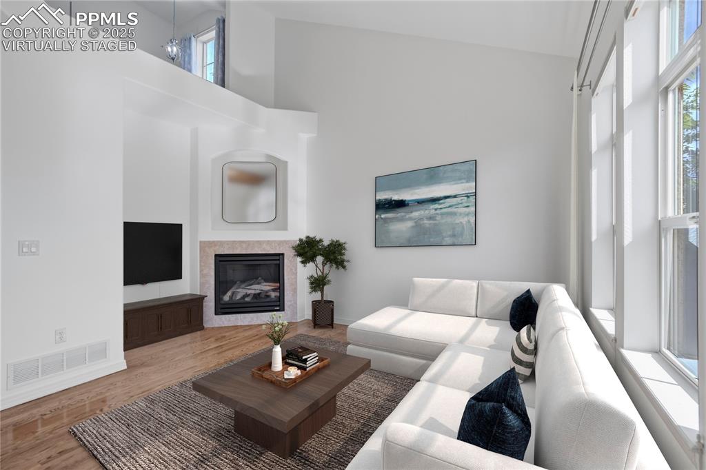Image 4 of 50: Living area with a towering ceiling, wood finished floors, and a glass cove