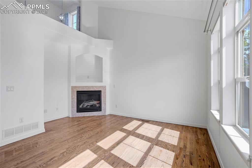 Image 47 of 50: Unfurnished living room with a high ceiling, wood finished floors, and a ti