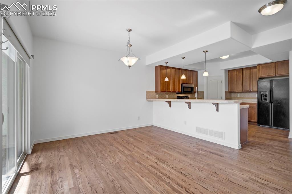 Image 48 of 50: Kitchen featuring brown cabinetry, black refrigerator with ice dispenser, a