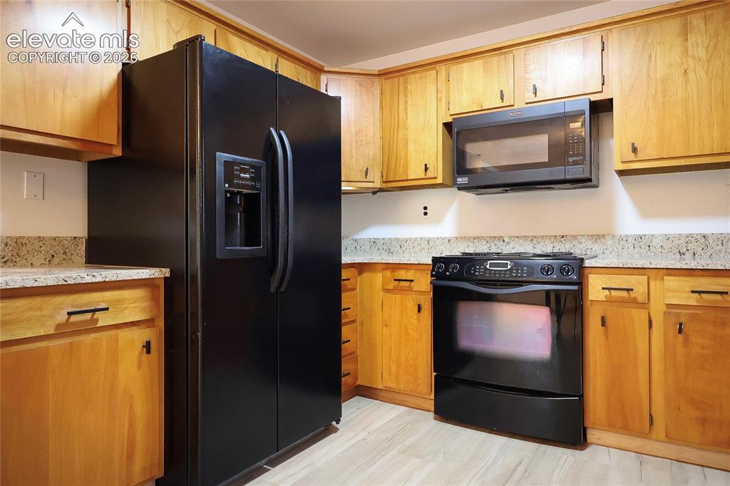 Image 14 of 40: Kitchen featuring wood cabinetry, black appliances, light-toned countertops