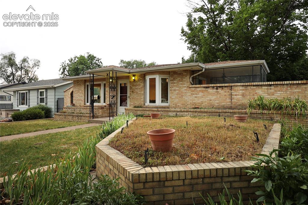Image 2 of 40: Brick facade with white-framed windows, an enclosed sunroom, and a covered